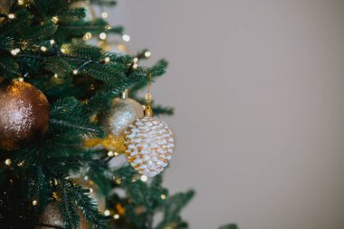 The Christmas tree features a variety of golden and silver ornaments, including a decorative pine cone, creating a festive atmosphere in a warmly lit living room during the holiday season. clipart