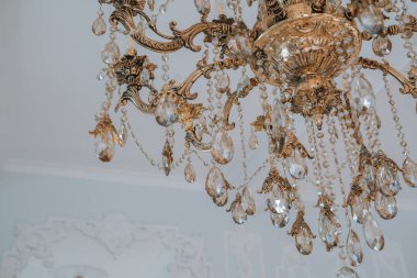 Tavandan sarkan parlak kristallerle süslenmiş güzel el yapımı klasik bir avize, yumuşak ışıklı bir odada sıcak bir parıltı bırakıyor. Tasarımın karmaşık ayrıntıları büyüleyici..