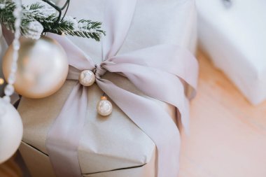 Zarif bir kurdele ve parlak süslemelerle süslenmiş açık renkli bir yüzeyde güzel bir hediye yatıyor. Şenlikli bir kutlamanın özünü yakalıyor, beklenti yaratıyor..