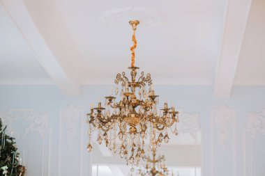 Göz kamaştırıcı bir kristal avize beyaz bir tavanda asılı, süslü detaylar ve parıldayan ışık yansımaları var. Tasarım, aydınlık odaya incelik ve cazibe katıyor..