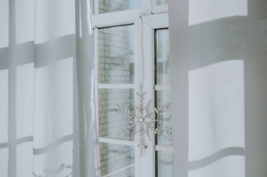 Yumuşak kış güneşi beyaz perdelerin arasından akar, pencerenin yanında asılı duran narin bir kar tanesi süsünü ortaya çıkarır, iç kısmın sıcak atmosferini yükseltir..