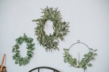 Doğal yapraktan yapılmış üç zarif yeşil çelenk, açık renkli bir duvara asılarak, iç mekanın cazibesini arttırıyor..