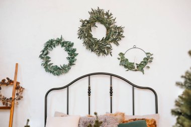 Three elegant wreaths made of greenery hang above a stylish black bed frame in a tranquil room, creating a soothing atmosphere with a touch of nature. clipart