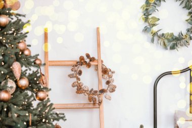 A cheerful holiday setting showcases a decorated Christmas tree and a rustic pinecone wreath hanging on a wooden ladder, enhancing the warm atmosphere of the room. clipart