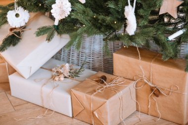 Renkli paketlenmiş hediyeler süslü bir Noel ağacının altında oturur, etrafı şenlikli süslemelerle çevrilidir. Sıcak atmosfer, tatil kutlamaları için beklenti yaratıyor..