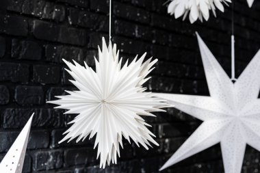 Elegant white paper stars dangle from above, creating a striking contrast against the dark brick wall. These decorations add a festive touch, perfect for holiday celebrations and gatherings. clipart