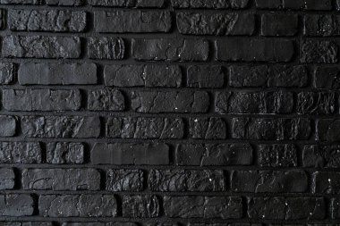 A solid black brick wall displays a rough, textured surface, enhancing the modern urban atmosphere. The unique patterns create an intriguing backdrop for various design applications. clipart