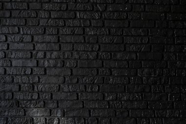 Resim siyah tuğlalı bir duvarın yakın çekimini gösteriyor. Derin renk ve desenli yüzey çeşitli tasarım uygulamaları veya sanatsal amaçlar için modern ve cesur bir arkaplan ekler.