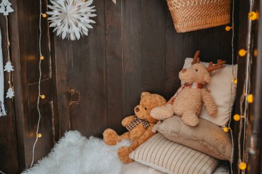 Yumuşak yastıklar ve battaniyelerin arasına yerleştirilmiş peluş oyuncak ayılar, şenlikli dekorasyonlar ve sıcak ışıklandırmalarla rahat bir kış kuyusu oluşturuyor..