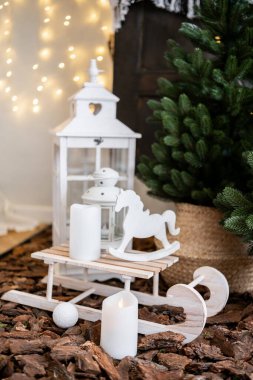 A charming holiday display featuring a white lantern, a wooden rocking horse, and candles set against a festive backdrop of twinkling lights and a pine tree. clipart