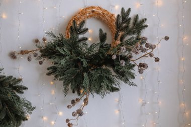 Güzelce hazırlanmış bir tatil çelengi yanıp sönen ışıklarla süslenmiş bir duvara asılır. Sergide yemyeşil çam dalları ve dekoratif elementler yer alıyor ve festival atmosferine cazibe katıyor..