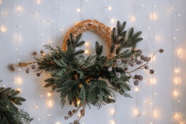 Güzel bir duvar dekorasyonu, taze yeşillik ve kış aksanıyla süslenmiş dairesel bir saman tabanı içerir. Yumuşak peri ışıkları arka planda parıldar, ılık, şenlikli bir atmosfer yaratır..