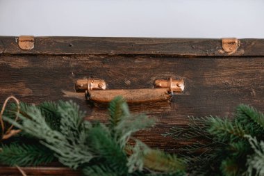 Bakır saplı eski ahşap bir sandık, sade bir arka fona dayanır, taze yeşil dallarla süslenir, rahat, mevsimsel bir atmosfer yaratır..