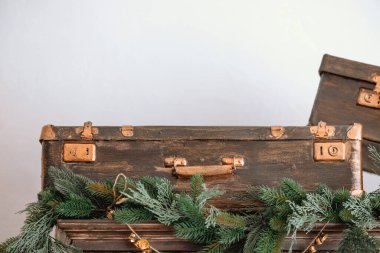 Kırsal ahşap bir bavul, canlı yeşil çelenkler ve küçük süslemelerle süslenmiş bir rafa konur. Tatil sezonu için rahat bir ortam yaratır..