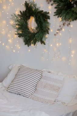 Rahat bir yatak odasında çizgili ve desenli yastıkla süslenmiş beyaz bir yatak vardır. Yeşil çelenkler ve parıldayan ışıklar sıcak, davetkar bir ortam yaratır. Tatil için mükemmel..