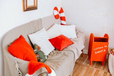 This inviting living room features a comfy sofa adorned with red and white pillows, alongside a cheerful mailbox for letters to Santa, creating a festive atmosphere for the holidays. clipart