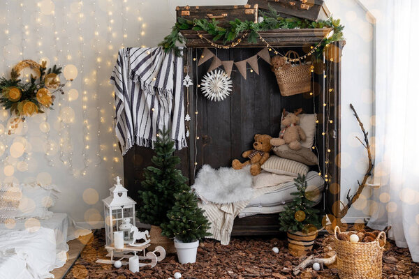 A charming corner showcases a dark wardrobe filled with decorative items, including teddy bears and small evergreen trees. Soft fabrics and warm lights create a cozy holiday atmosphere.