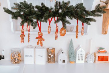 Çekici bir mutfakta Noel süsleri ve baston şekerlerle süslenmiş bir çelenk bulunur. Aşağıda, şeker dolu kavanozlar ve dekoratif evler tatil ruhunu canlandırıyor..