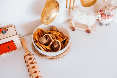 A decorative bowl holds dried orange slices and nuts, adding warmth to the cozy kitchen. Surrounding elements include a rolling pin and charming kitchen decor pieces, enhancing the ambiance. clipart