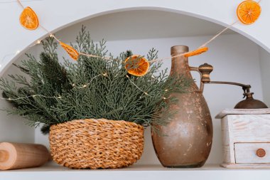 A charming kitchen shelf displays a woven basket filled with green foliage, dried orange slices hanging as decoration, and rustic kitchen items adding warmth to the space. clipart