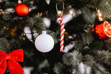 Şenlikli bir Noel ağacı, beyaz top ve kırmızı şeker kamışı da dahil olmak üzere çeşitli renkli süslemelerle süslenir. Parlak ışıklar yeşilliği aydınlatır ve sıcak bir tatil atmosferi yaratır..