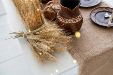 A warm and inviting winter setting features a beautifully arranged table with wheat, rustic pottery, and baked goods, perfect for holiday celebrations and family gatherings. clipart