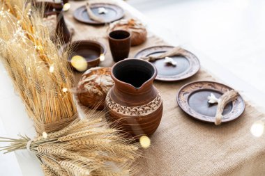 Güzel düzenlenmiş bir yemek masasında kırsal çömlek, kahverengi ekmek ve dekoratif buğday bulunur. Sahne, bir Noel kutlamasının sıcaklığını yakalıyor ve toplanmak için samimi bir atmosfer vurguluyor..