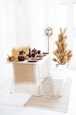 Çok güzel düzenlenmiş bir kış sofrasında kırsal çömlekler ve doğal elementler mevcuttur, sıcak bir Noel kutlaması için mükemmeldir ve 2025 yılını aydınlık, havadar bir mekanda karşılar..