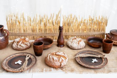 Sıcak bir kış masası kırsal ekmek, ahşap tabaklar ve fincanlarla süslenir. Arka planda buğday dekoru, Noel ve Yeni Yıl kutlamaları için sıcak bir atmosfer yaratıyor.