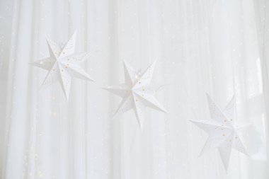 Beyaz kağıt yıldızlar, yumuşak bir kış arkaplanına karşı zarifçe asılıp Noel ve yeni yıl kutlamaları için atmosfere şenlikli bir dokunuş eklenmiştir..