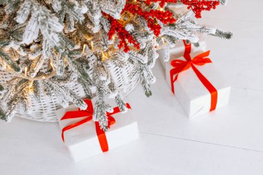 Güzel dekore edilmiş bir Noel ağacının altında kırmızı kurdeleli beyaz hediye kutuları karlı bir zeminde oturur ve sıcak bir kış ortamı yaratır. Sahne, tatil sezonunun ruhunu yansıtıyor..
