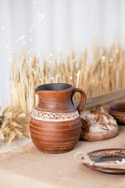 Kır çömleği, pişirilmiş ekmek ve geleneksel seramik tabaklarla süslenmiş kış temalı bir masada zarif bir şekilde oturur ve Noel ve yeni yıl kutlamalarının sıcak özünü yakalar..