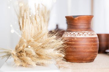 Dekoratif elementler, kışın sıcacık atmosferini ön plana çıkararak, güzel düzenlenmiş kuru buğdayın yanında kırsal bir çömlek sergiliyor. Bayram havası yaratmak için mükemmel..