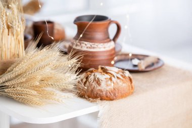 A beautifully arranged winter table includes a rustic bread loaf, ceramic pitcher, and wheat decor, creating a warm atmosphere for Christmas and New Year festivities. clipart