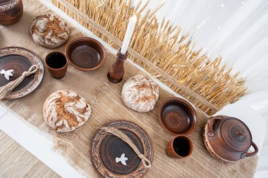 Güzelce düzenlenmiş bir kış masasında tabaklar, fincanlar ve çaydanlık da dahil olmak üzere kırsal çömlekler yer alır. Doğal elementler ve bir mum ile süslenmiş, sıcak bir Noel toplantısı için mükemmel..