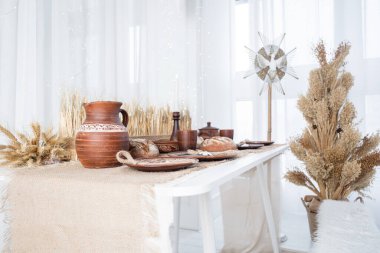 Sıcak bir kış sahnesinde geleneksel çömlek, fırın ürünleri ve kurutulmuş bitkilerle dolu bir köy masası sıcak bir tatil atmosferi yaratıyor..