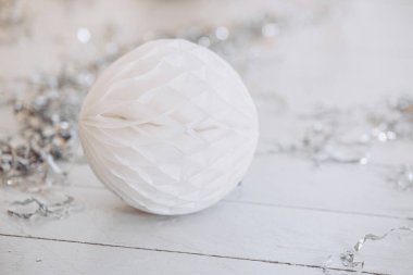 A soft white paper ornament rests on a wooden surface, accented by scattered silver tinsel. This charming decoration captures the essence of Christmas and New Year celebrations. clipart