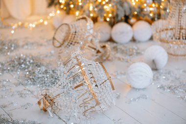 Silver and white decorations lie scattered on the floor near a sparkling Christmas tree. Twinkling lights and winter ambiance create a warm and joyful holiday atmosphere, perfect for celebrations. clipart