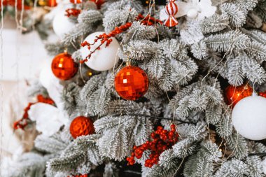 Güzel dekore edilmiş bir Noel ağacında kırmızı ve beyaz süsler, çam dalları ve şenlikli aksanlar yer alır. Bu kış ayarı Noel ve yeni yıl kutlamalarının ruhunu yansıtıyor..