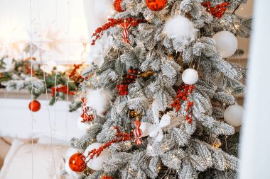 Güzel süslenmiş bir Noel ağacında canlı kırmızı süsler, kabarık beyaz aksanlar ve parlak ışıklar bulunur. Bu şenlikli gösteri, tatil ruhunu kutlayan sıcak bir atmosfer yaratıyor..