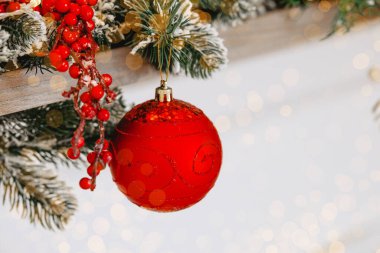 Meyve ve yeşillikle süslenmiş, kar tozlu bir çelenkten sarkan canlı kırmızı bir süs. Bu büyüleyici görüntü Noel ve Yeni Yıl kutlamalarının özünü yansıtıyor..