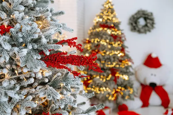 Işıklar ve kırmızı aksanlarla süslenmiş iki güzel Noel ağacı kış arkaplanına karşı duruyor. Şenlikli hediyeler ve sıcak bir ayı neşeli tatil atmosferine katkı sağlar..