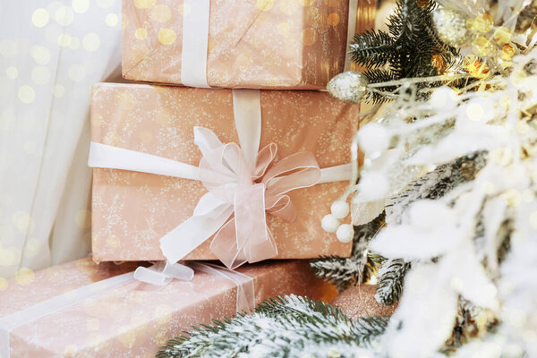 Wrapped gifts in elegant pastel colors are stacked under a decorated Christmas tree. The scene conveys a warm, festive atmosphere, perfect for celebrating the holiday season.