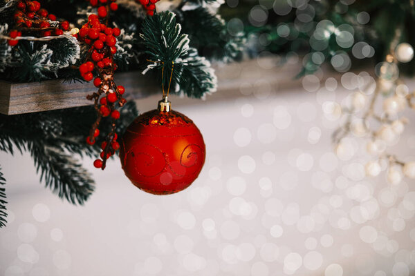 A vibrant red ornament dangles from lush evergreen branches adorned with berries.