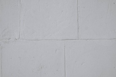 Kalıplaşmış gri bir duvar, gün ışığında ışığı yansıtan ince varyasyonlar gösterir. Basit tasarım, bu minimalist ortamda mimarinin pratik yönlerini vurgular..