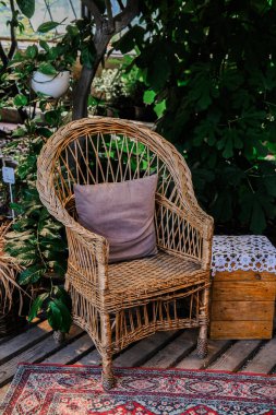 Yumuşak yastıklı büyüleyici bir hasır sandalye huzurlu bir bahçedeki yemyeşil bitkilerin arasına davetkar bir şekilde oturur. Doğal ahşap zemin ve dekoratif elementler dingin atmosferi arttırır, rahatlamak için mükemmeldir..