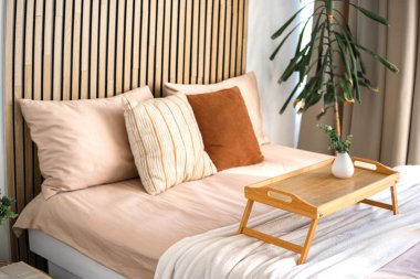 Rahat bir yatak odasında yumuşak yastıkları ve tepsisi olan ahşap bir yatak başlığı vardır..