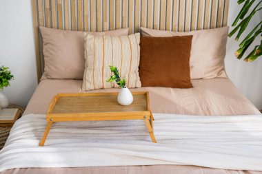 Sıcak ve davetkar bir yatak odası düzgün düzenlenmiş bir yatakta ahşap bir tepsi içerir..