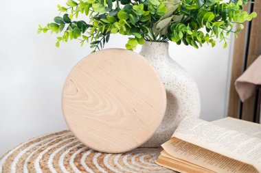 Basit bir ahşap bardak altlığı yeşil bir bitki ve açık bir masanın üzerinde duruyor..