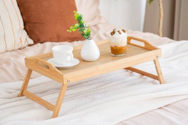 Sıcak bir kahvaltı tepsisi, güneş ışığında yumuşak bir yatakta kahve ve tatlı tutar..